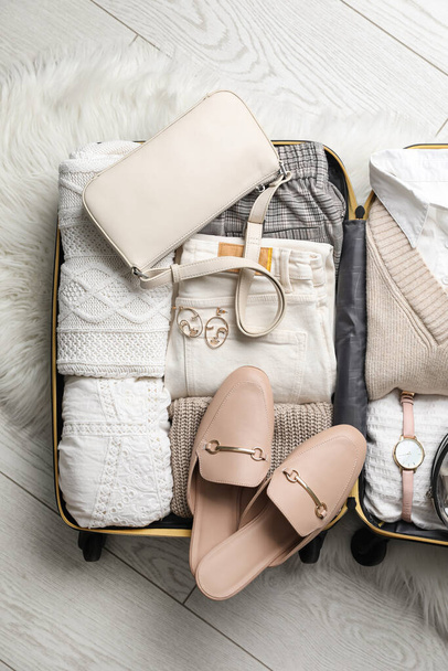 Open suitcase with folded clothes, shoes and accessories on floor, top view - Foto, afbeelding