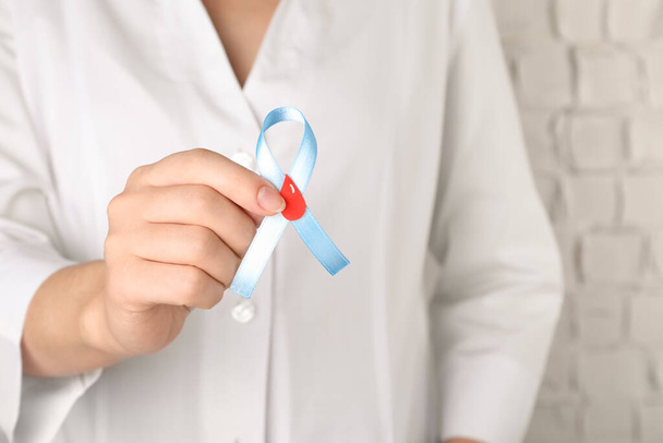 Doctor holding light blue ribbon with paper blood drop, closeup. World Diabetes Day - Foto, Bild