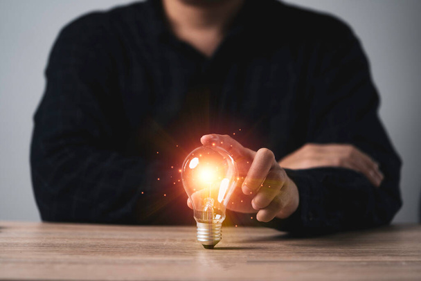 Homme d'affaires tenant ampoule lumineuse avec rayon de lumière orange sur la table en bois pour l'inspiration idée de pensée créative et concept de technologie d'innovation future. - Photo, image