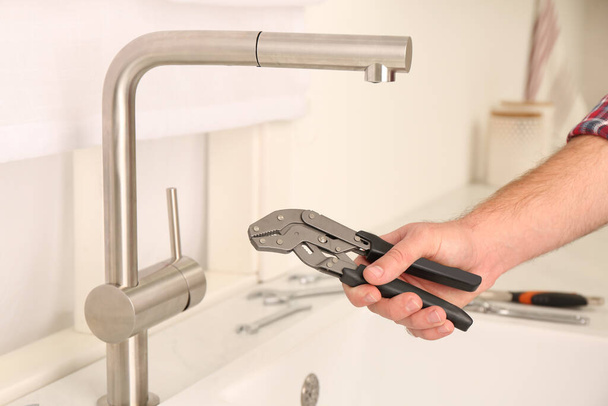 Man with wrench near sink in kitchen, closeup. Water tap installation - Foto, imagen