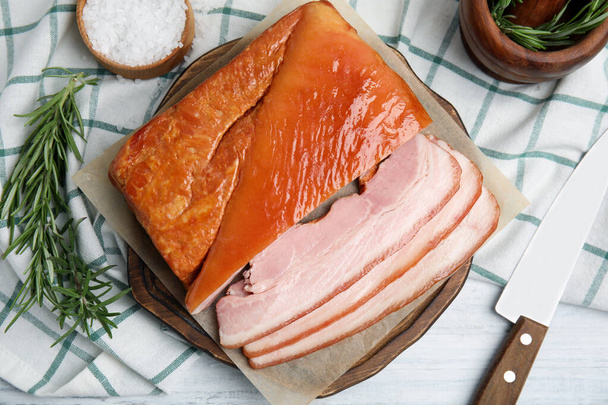 Delicious smoked bacon with rosemary and salt on white wooden table, flat lay - Foto, afbeelding