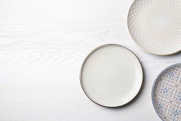 Three beautiful plates on white wooden table, flat lay. Space for text - Zdjęcie, obraz