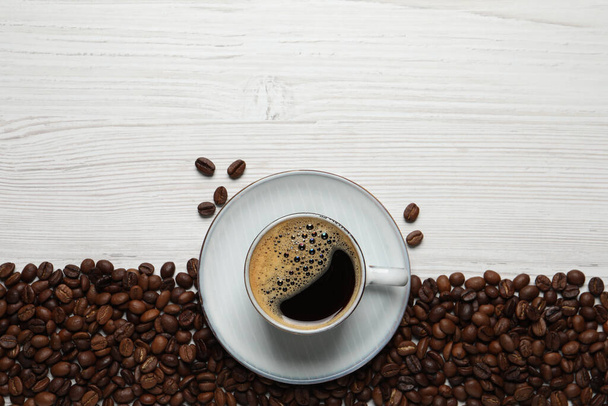 Cup of aromatic hot coffee and beans on white wooden table, flat lay. Space for text - Photo, image