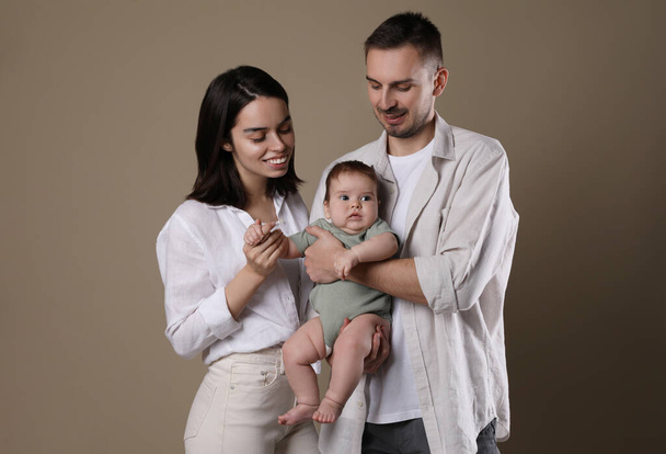 Happy family. Couple with their cute baby on beige background - Фото, зображення