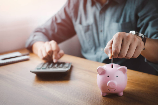 Ein Mann steckt Münzen in ein rosafarbenes Sparschwein, um Geld zu sparen. Planung vorantreiben, Geld sparen für Zukunftspläne, Altersvorsorge. Konzept der Unternehmensfinanzierung für die Buchführung. - Foto, Bild