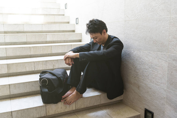 Conceito de fracasso de negócios: Jovens empresários sentam-se nas escadas e suas mãos apertam os joelhos Porque ele está tão desesperado, estressado, tristeza depois de saber a má notícia de que ele está desempregado. - Foto, Imagem