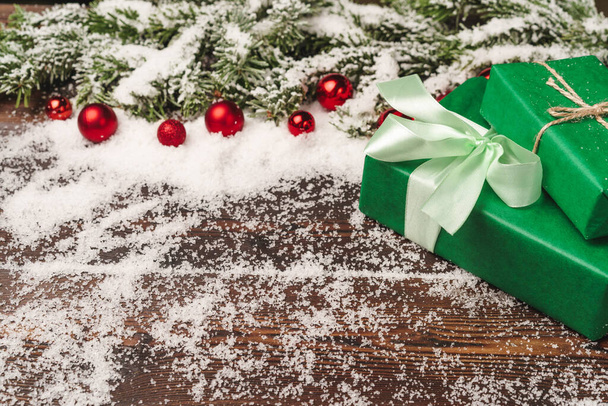 Presents on wooden background with fir tree branches and red baubles powdered with snow - Fotografie, Obrázek