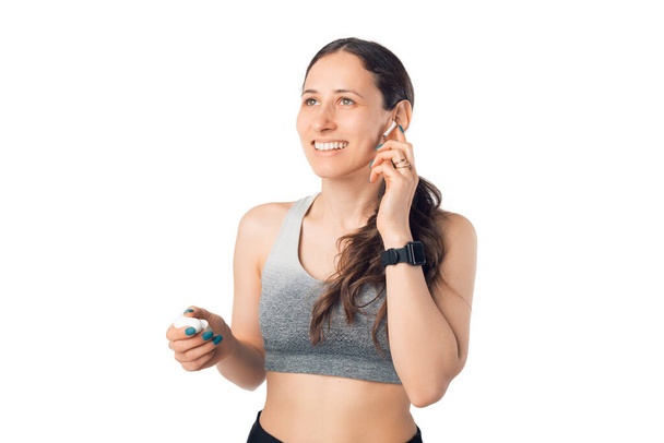 Wide smiling girl is using her ear pods while practicing sports. Photo over white background. - Foto, imagen