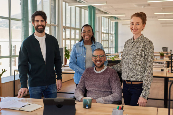 Diverse group of young of businesspeople smiling while working together at a desk in modern open plan office space - 写真・画像