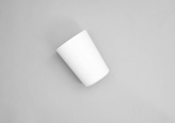a cup in oblique position from top point of view. minimal shot for simple mockup. white plastic cup on grey background. realistic mockup for promotion. - Foto, Imagen