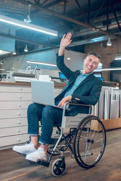 Man in wheelchair welcomingly raising hand in office - Foto, immagini