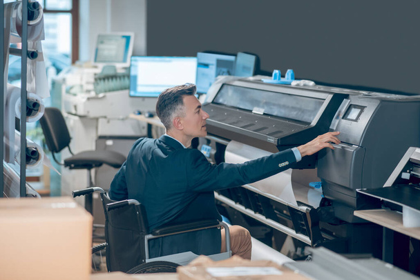 Perfil del hombre en silla de ruedas tocando paneles de control de impresora - Foto, Imagen