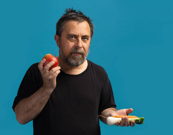 Egészséges életmód és vegetáriánus. Egy középkorú férfi fekete pólóban gyümölcsöt és zöldséget tart a kezében. - Fotó, kép