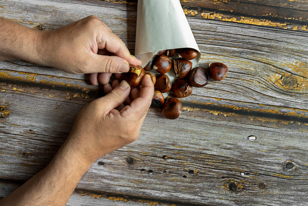 Ręce człowieka obierają kasztany z kornetu pełnego pieczonych kasztanów w chłodny zimowy dzień - Zdjęcie, obraz