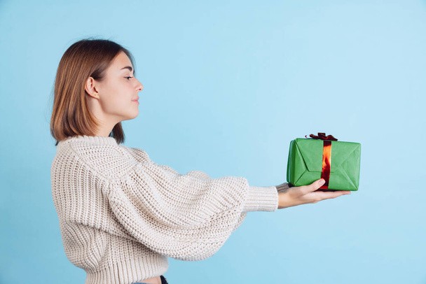 Portrait of young girl, teen or student in casual clothes holding New Year gift box isolated on blue studio backgroud. - Foto, imagen
