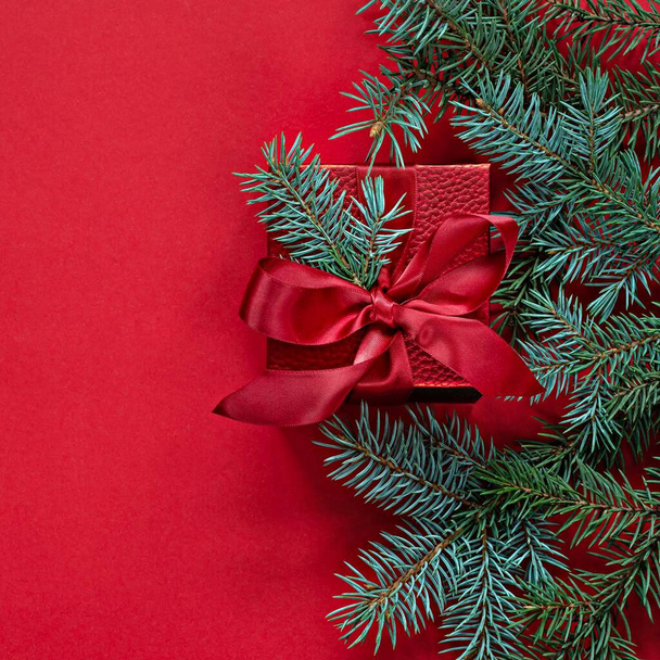Feestelijke rode geschenkdoos met sparren takken op een rode achtergrond. Kerst- en nieuwjaarsconcept, vakantie, kopieerruimte. - Foto, afbeelding