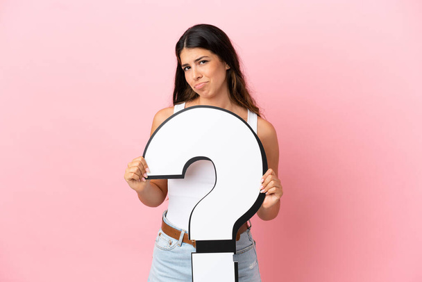 Young caucasian woman isolated on pink background holding a question mark icon and with sad expression - Photo, Image