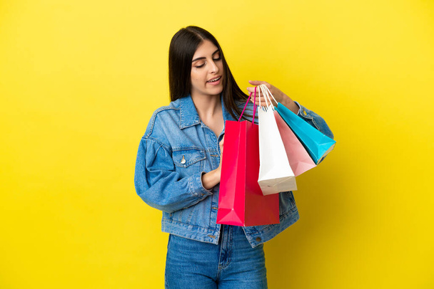Young caucasian woman isolated on blue background holding shopping bags - Foto, afbeelding