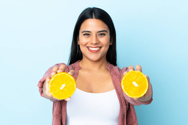 Junge lateinische Frau isoliert auf blauem Hintergrund mit einer Orange - Foto, Bild