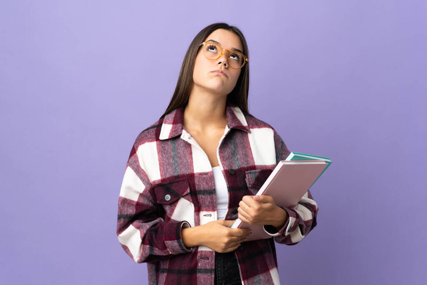 Young student woman isolated on purple background and looking up - Photo, Image