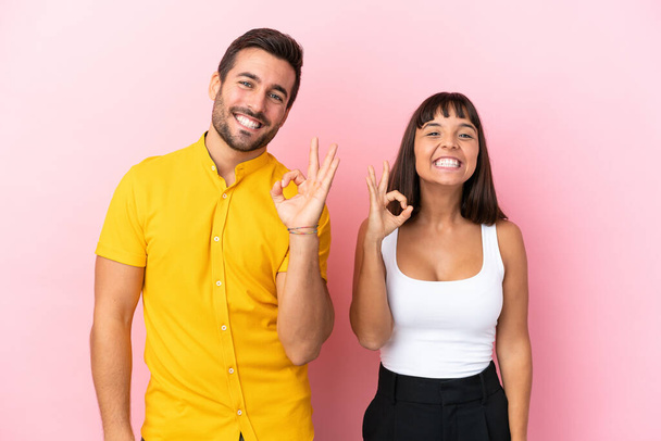 Νεαρό ζευγάρι απομονώνονται σε ροζ φόντο δείχνει μια πινακίδα εντάξει με τα δάχτυλα - Φωτογραφία, εικόνα