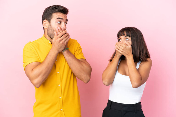Young couple isolated on pink background covering mouth with hands for saying something inappropriate - Φωτογραφία, εικόνα