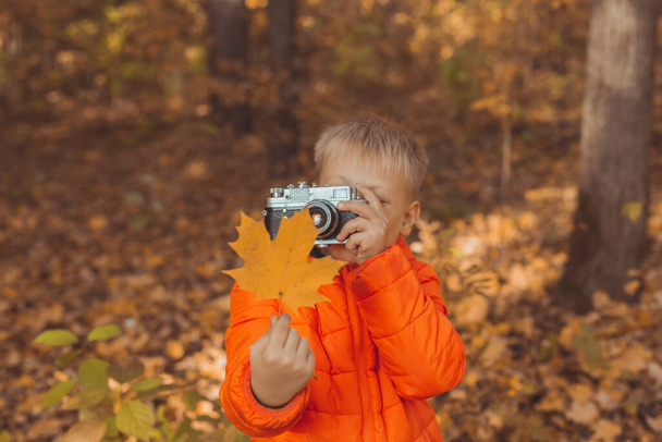 秋の自然の中で屋外で写真を撮るレトロカメラを持つ少年。レジャーと写真家のコンセプト - 写真・画像