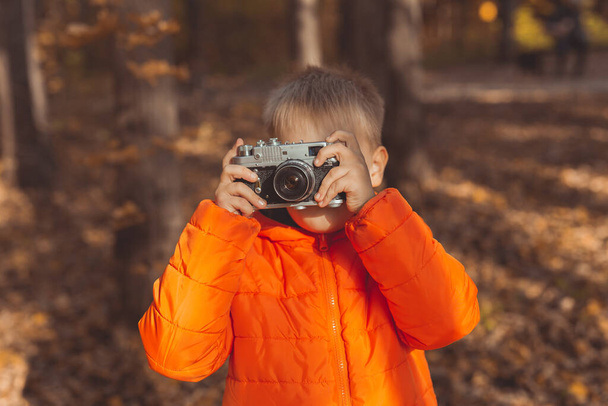 Niño con cámara retro tomando fotos al aire libre en la naturaleza de otoño. Concepto de ocio y fotógrafos - Foto, Imagen