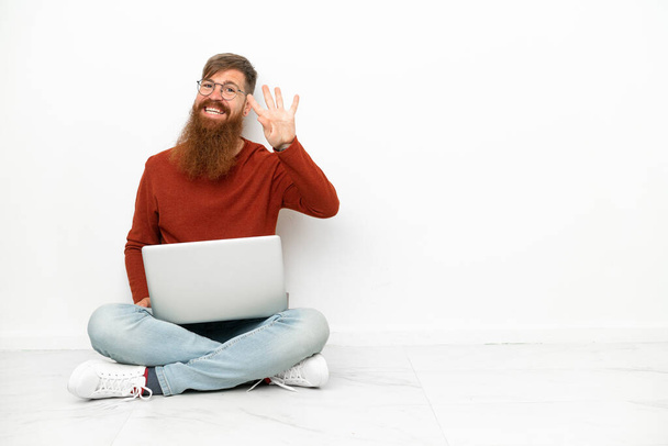 Jeune homme caucasien rougeâtre avec ordinateur portable isolé sur fond blanc heureux et comptant quatre avec des doigts - Photo, image