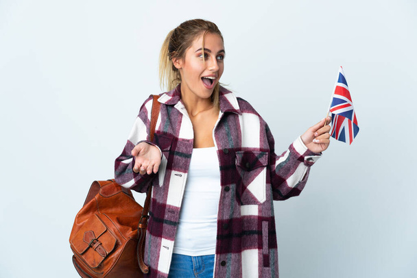 Jovem segurando uma bandeira do Reino Unido isolada no fundo branco com expressão surpresa enquanto olha para o lado - Foto, Imagem