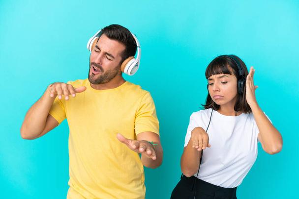 Young couple isolated on blue background listening music and dancing - Photo, Image