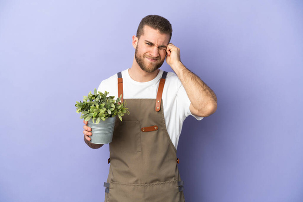 Gardener caucasian man holding a plant isolated on yellow background frustrated and covering ears - Fotoğraf, Görsel