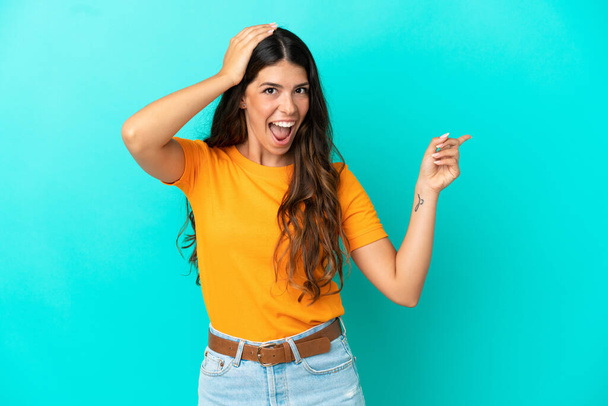 Young caucasian woman isolated on blue background surprised and pointing finger to the side - Foto, Imagem