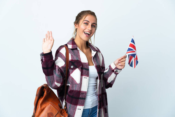 Junge Frau mit britischer Flagge auf weißem Hintergrund salutiert mit fröhlichem Gesichtsausdruck - Foto, Bild
