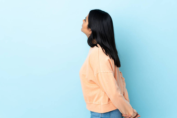 Молода жінка з Латинської Америки ізольована на синьому фоні в положенні спини і дивиться назад
 - Фото, зображення