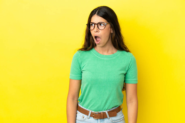 Young caucasian woman isolated on yellow background doing surprise gesture while looking to the side - Foto, Bild