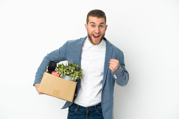 Young caucasian making a move while picking up a box full of things isolated on white background celebrating a victory in winner position - Photo, Image