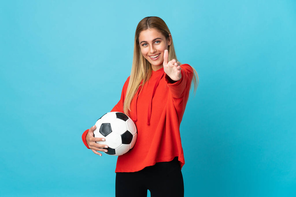 Joven futbolista mujer aislada sobre fondo azul estrechando las manos para cerrar una buena oferta - Foto, Imagen