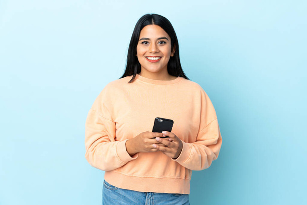 Молодая латиноамериканка, изолированная на синем фоне, отправляет сообщение с мобильником
 - Фото, изображение