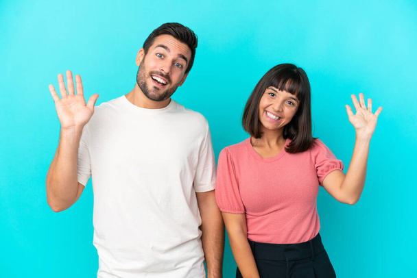 Νεαρό ζευγάρι απομονωμένο σε μπλε φόντο χαιρετισμό με το χέρι με χαρούμενη έκφραση - Φωτογραφία, εικόνα