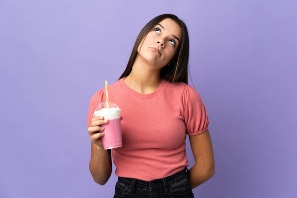 Девочка-подросток держит клубничный молочный коктейль и смотрит вверх - Фото, изображение