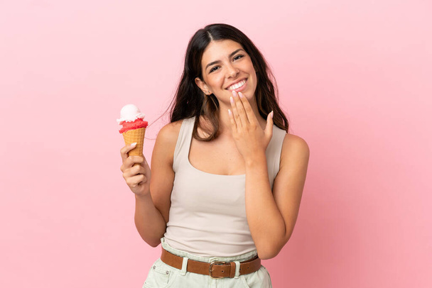 Young caucasian woman with a cornet ice cream isolated on pink background looking up while smiling - Фото, изображение