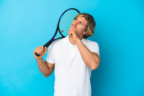blondýny tenista muž izolovaný na modrém pozadí a vzhlíží - Fotografie, Obrázek