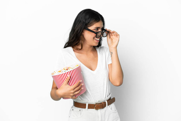 Young caucasian woman isolated on white background with 3d glasses and holding a big bucket of popcorns - Fotó, kép