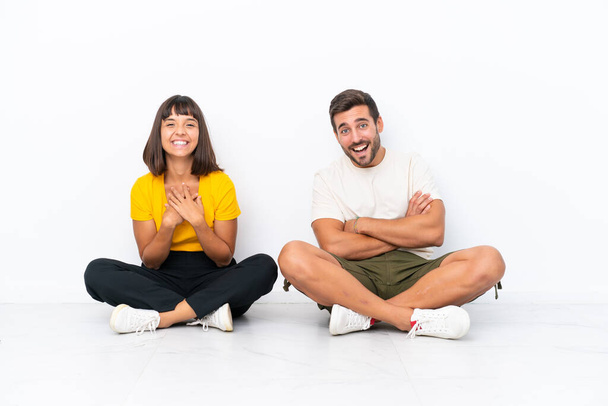 Young couple sitting on the floor isolated on white background keeping the arms crossed while smiling - Fotoğraf, Görsel