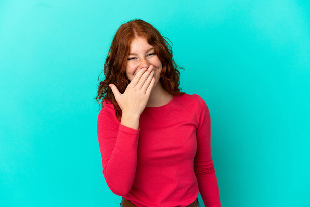Έφηβη κοκκινωπή γυναίκα απομονωμένη σε μπλε φόντο χαρούμενη και χαμογελαστή που καλύπτει το στόμα με το χέρι - Φωτογραφία, εικόνα