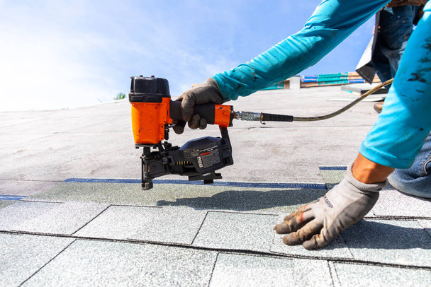 roofer installing roof shingles with pneumatic roofing nailer. - Photo, Image