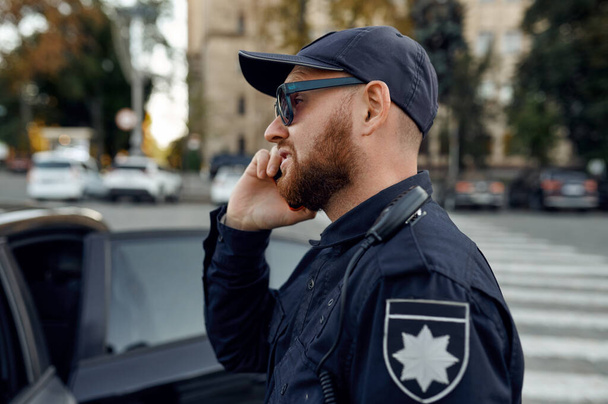 Офицер полиции разговаривает по телефону, автостоянка - Фото, изображение