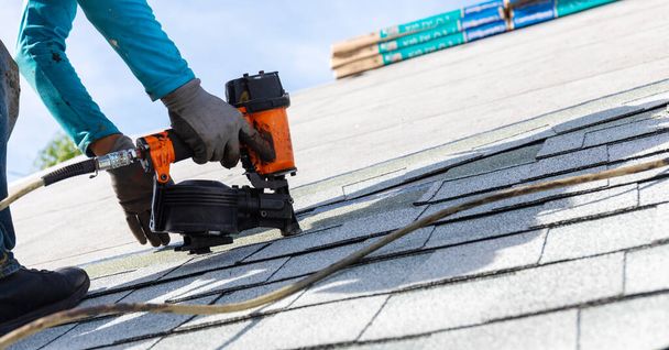 roofer installing roof shingles with pneumatic roofing nailer. - Photo, Image