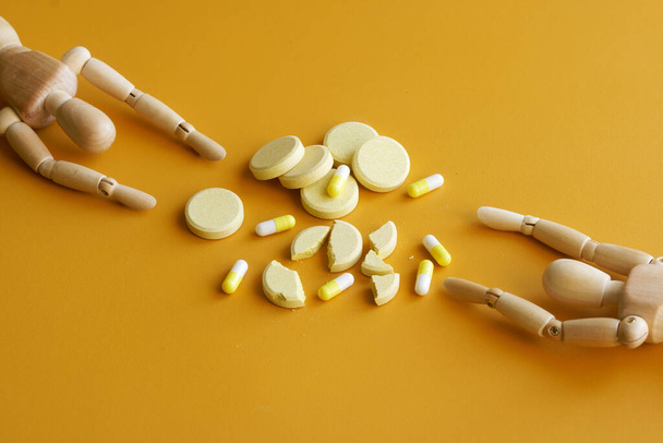 Monet pillerit ja pillerit vetävät puoleensa kahta ihmisnukkea. Huumeriippuvuuden käsite, toipumishalu ja huumepula. Keltainen tausta - Valokuva, kuva